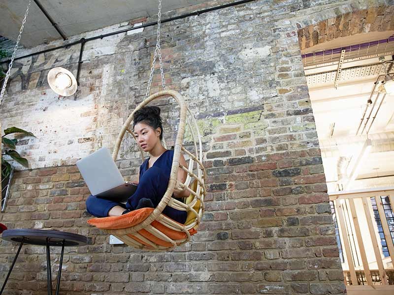 Women sitting on hanging chair and working on a laptop in office area